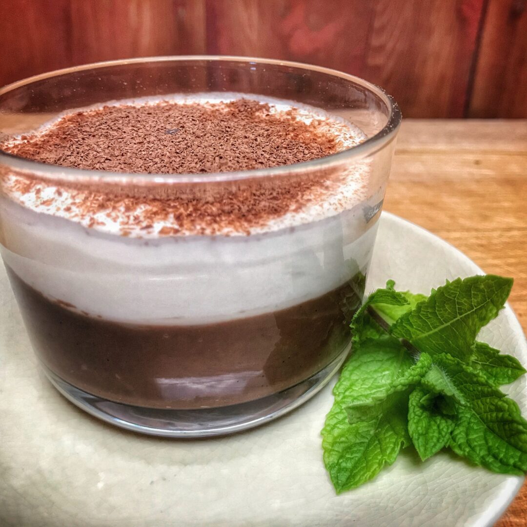 A glass of chocolate mousse with whipped cream and mint leaves.