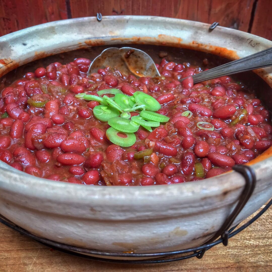 A bowl of chili beans topped with baby back ribs on a wooden table.
