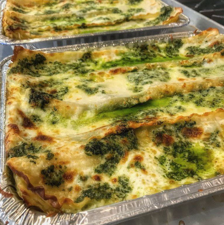 Two lasagnas with spinach and cheese on top of a stove.