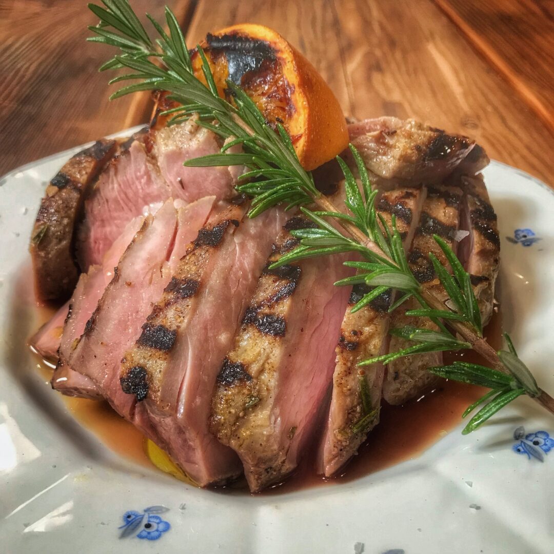 A plate of roasted pork with rosemary sprigs on it.