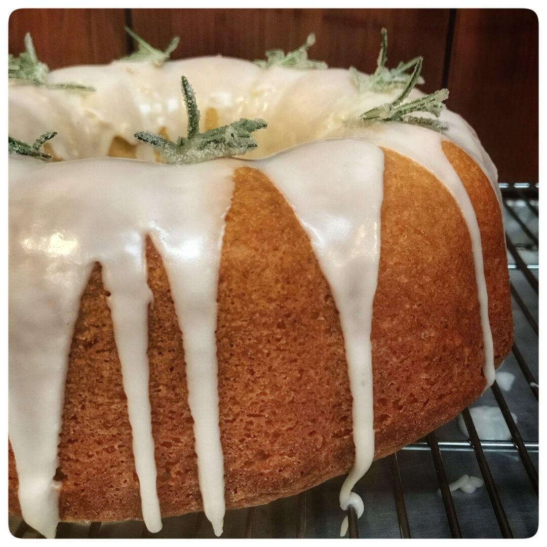A bundt cake with icing and sprigs of rosemary.