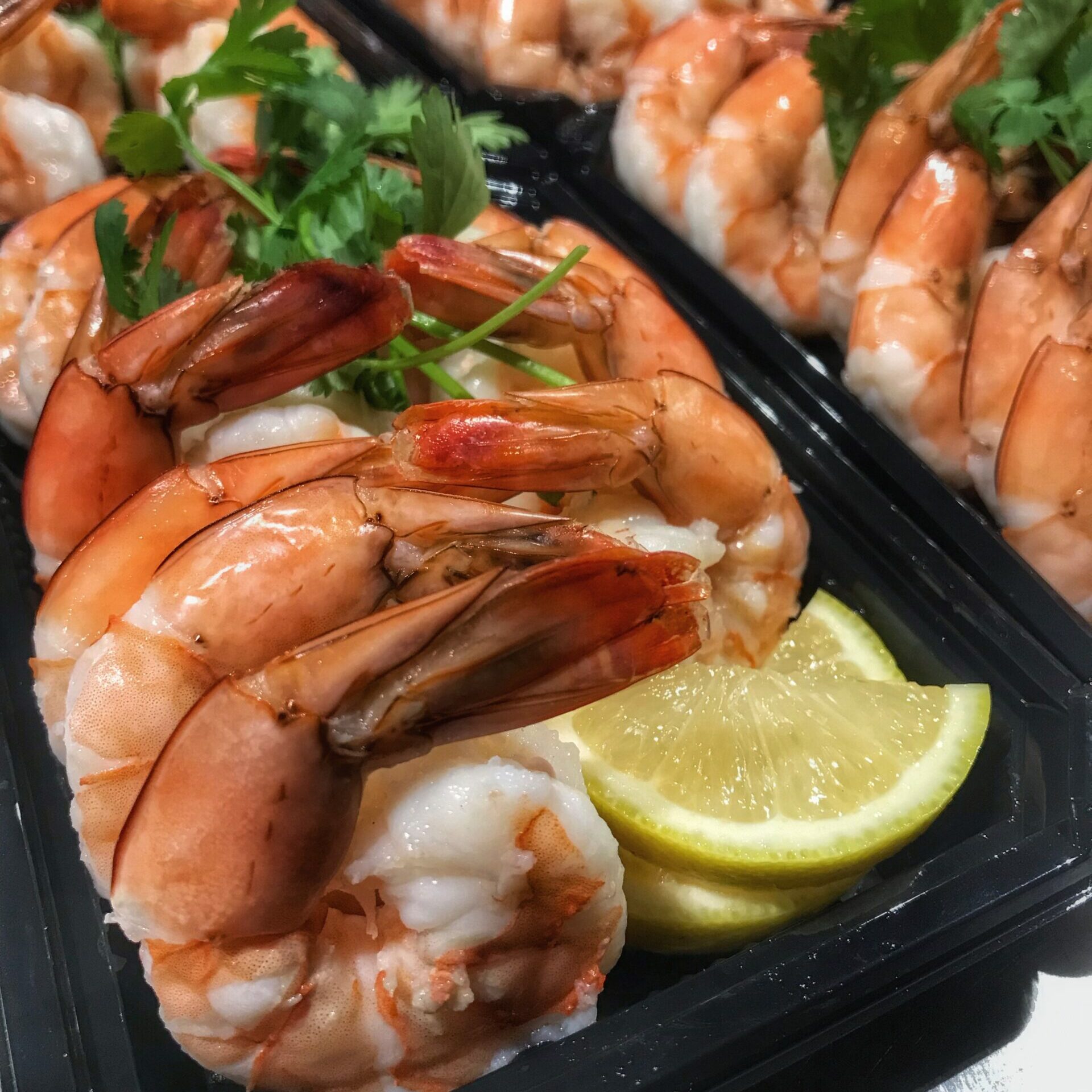 Prawns in black plastic containers with lemon wedges.