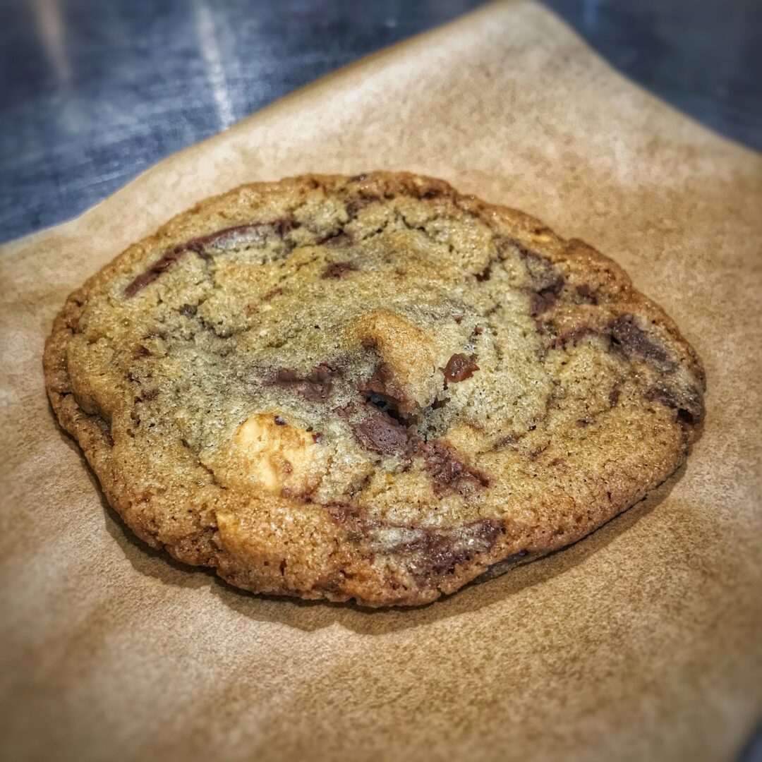 A chocolate chip cookie sitting on a piece of paper.
