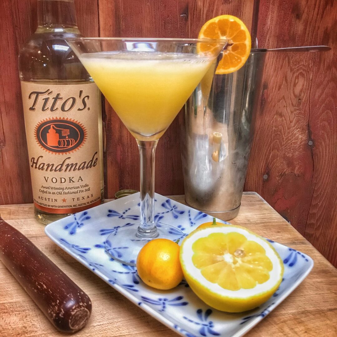 A martini glass with lemon slices and a bottle of tito's tequila.