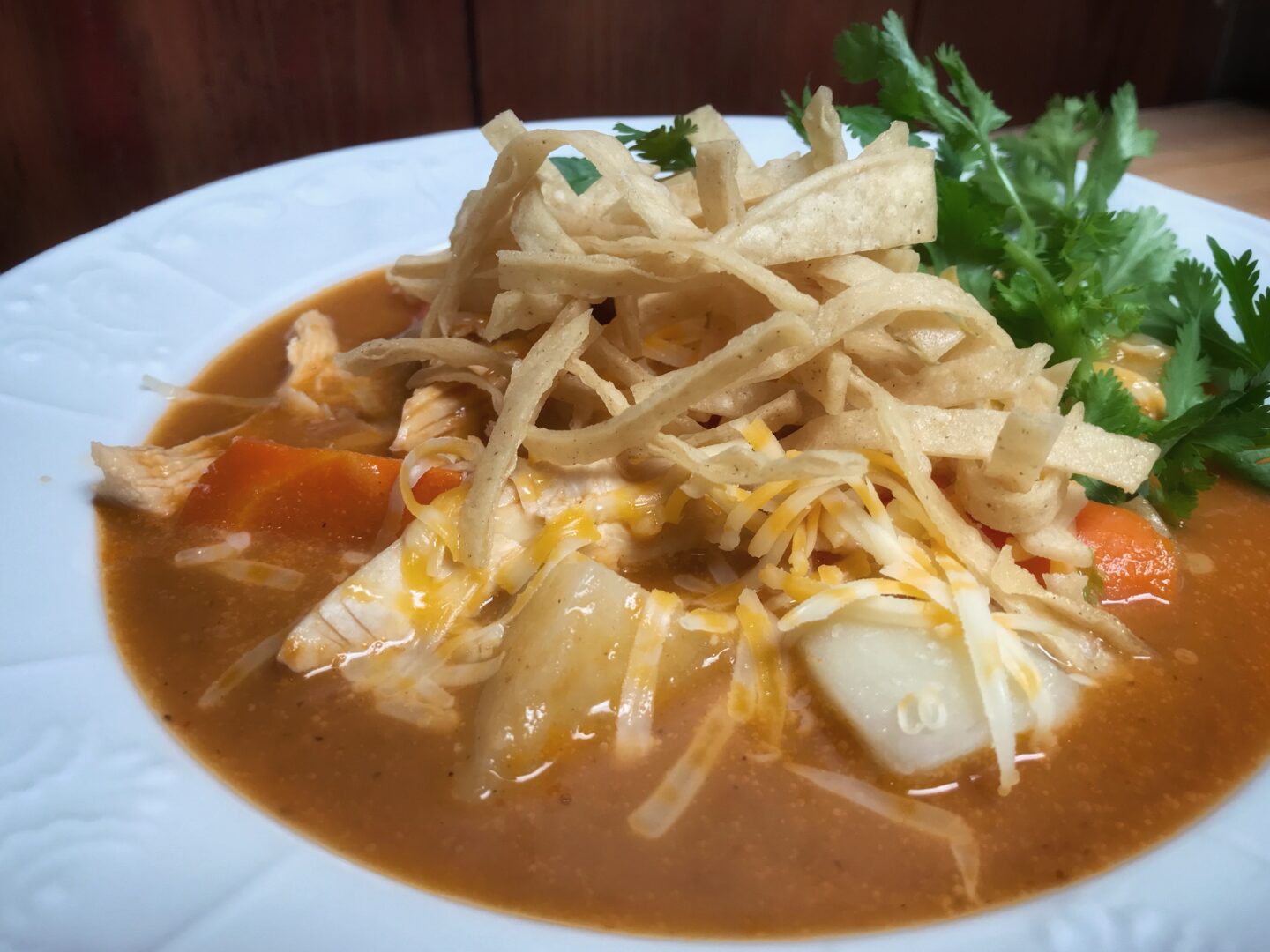 A white plate with a bowl of soup and tortillas.