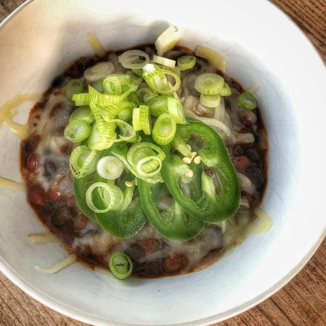 A bowl of chili with cheese and green onions.