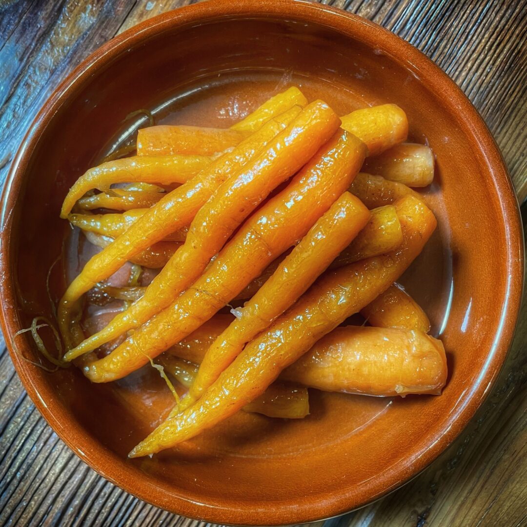 A bowl of carrots sitting on a wooden table.