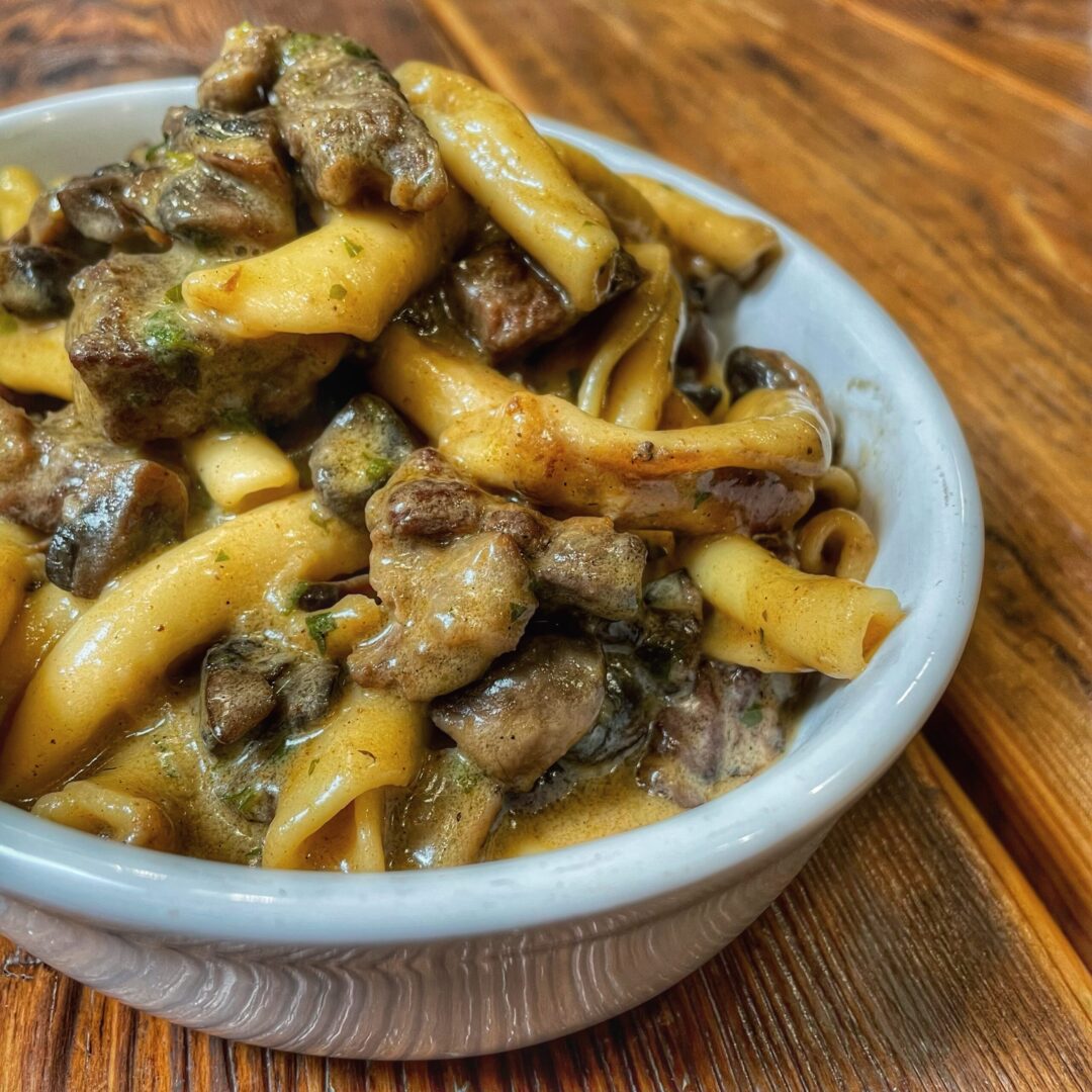 A bowl of pasta with meat and mushrooms.
