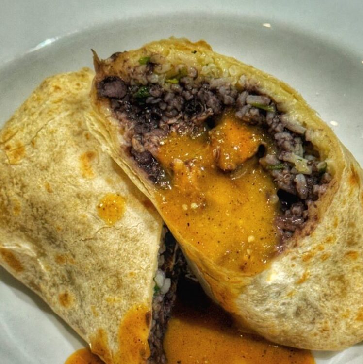Burrito cut in half to reveal filling, served with sauce.